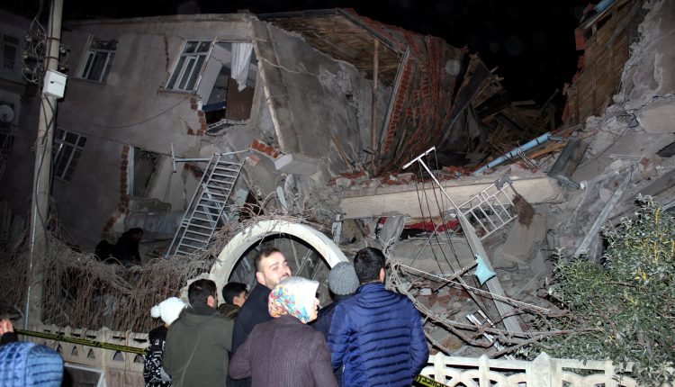 People stand outside a collapsed building after an earthquake in Elazig